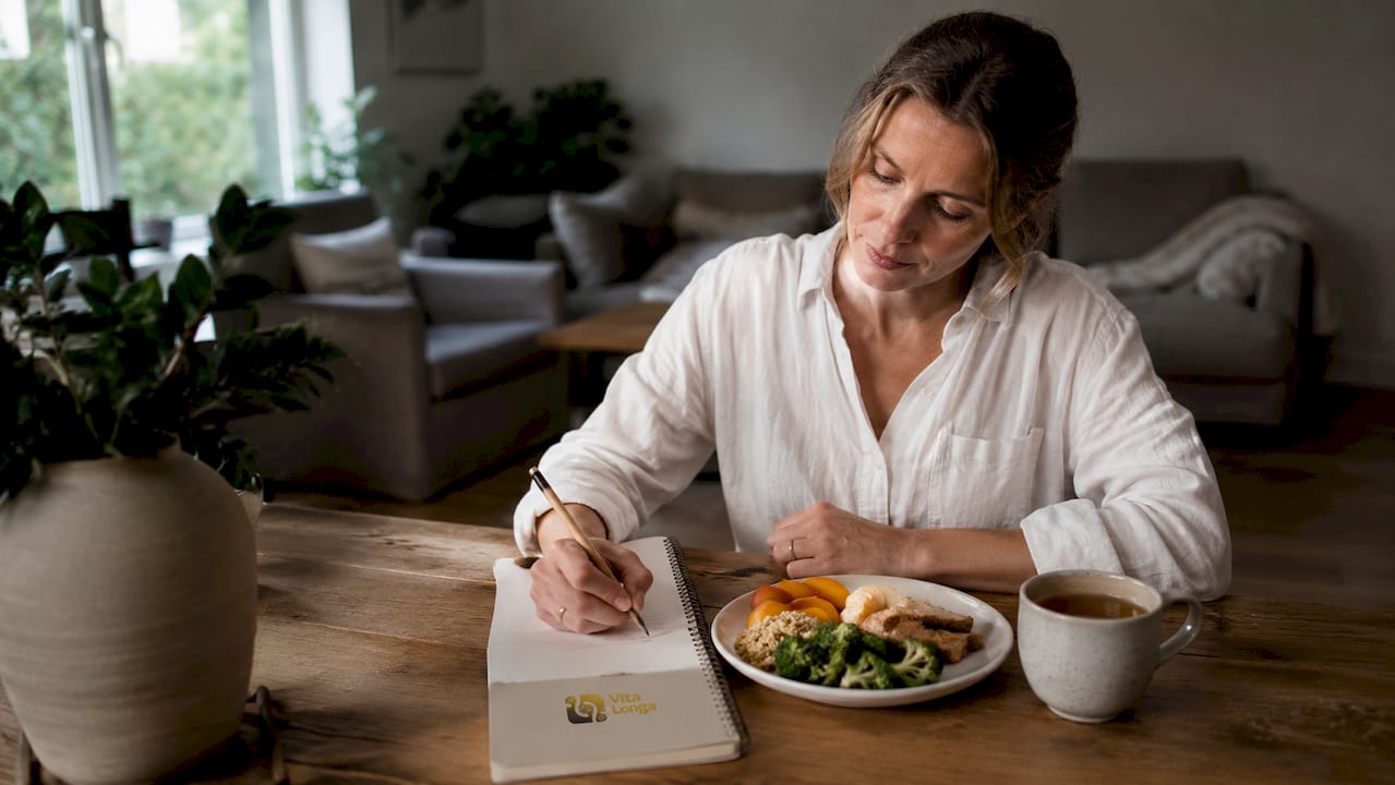 En kvinde sidder ved spisebordet og lægger en kostplan, der skal hjælpe mod hendes mavesår.